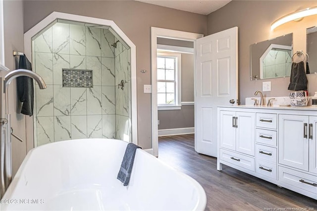 full bathroom featuring double vanity, baseboards, a soaking tub, wood finished floors, and a sink