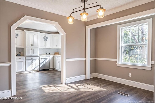 unfurnished dining area featuring dark wood-style flooring, crown molding, visible vents, a textured ceiling, and baseboards