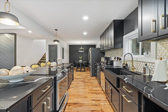 kitchen featuring pendant lighting, stainless steel appliances, decorative backsplash, light wood-style floors, and a sink