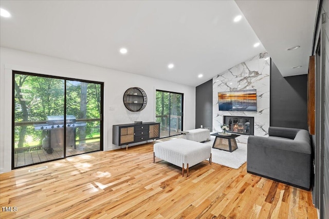 living area featuring lofted ceiling, recessed lighting, light wood finished floors, and a premium fireplace