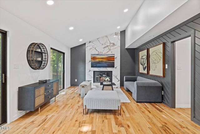 living area with vaulted ceiling, recessed lighting, a high end fireplace, and light wood-style floors