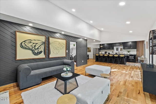 living room featuring wood walls, light wood-style flooring, high vaulted ceiling, and recessed lighting