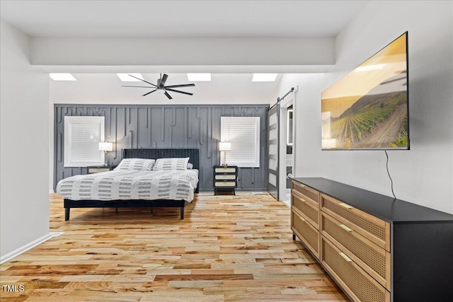 bedroom featuring a skylight, a barn door, baseboards, and light wood-style flooring