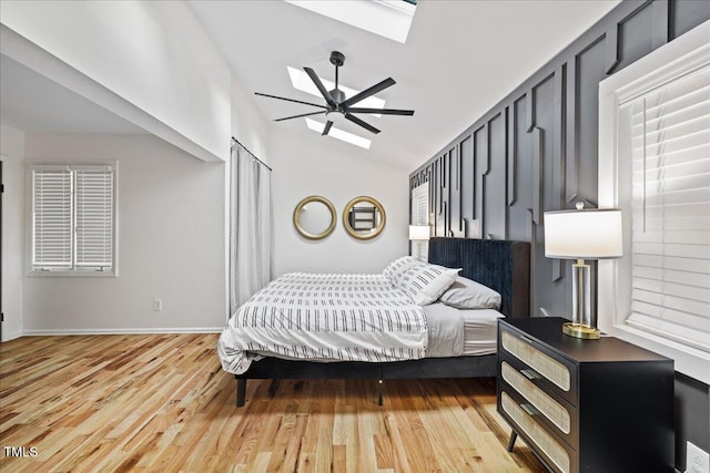 bedroom with baseboards, ceiling fan, lofted ceiling with skylight, and light wood-style floors