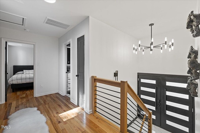 hall featuring baseboards, visible vents, an upstairs landing, and wood finished floors