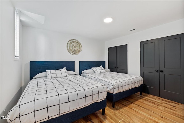 bedroom featuring light wood-type flooring, visible vents, and multiple closets