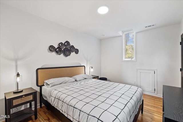 bedroom with baseboards, visible vents, and wood finished floors