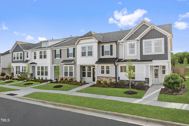 townhome / multi-family property with stone siding, metal roof, a front lawn, and a standing seam roof