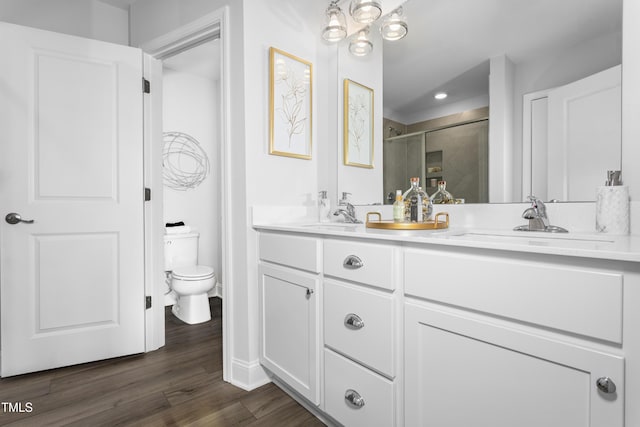 full bathroom with toilet, wood finished floors, a sink, a shower stall, and double vanity