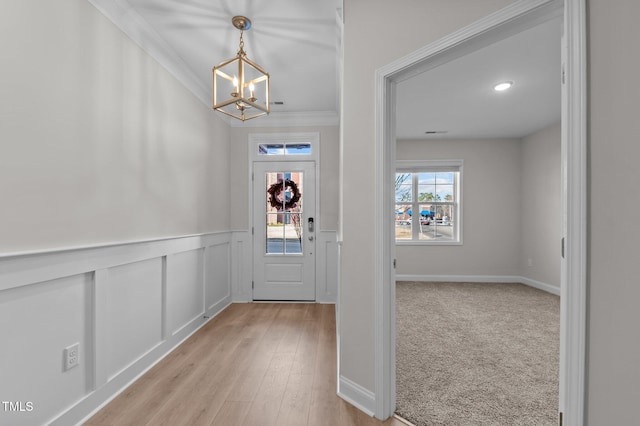 entrance foyer featuring a wainscoted wall, a decorative wall, ornamental molding, a chandelier, and light wood-type flooring