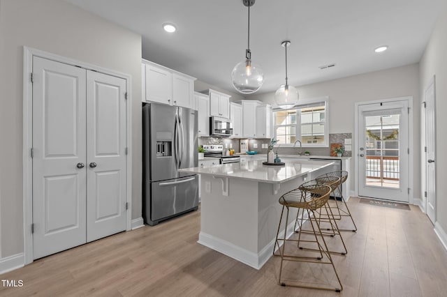 kitchen featuring tasteful backsplash, appliances with stainless steel finishes, light wood-type flooring, a kitchen bar, and white cabinetry