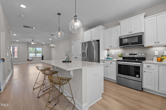 kitchen featuring stainless steel appliances, white cabinetry, visible vents, open floor plan, and decorative backsplash