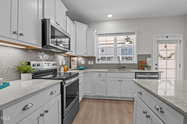 kitchen with stainless steel appliances, a sink, white cabinetry, light wood finished floors, and tasteful backsplash