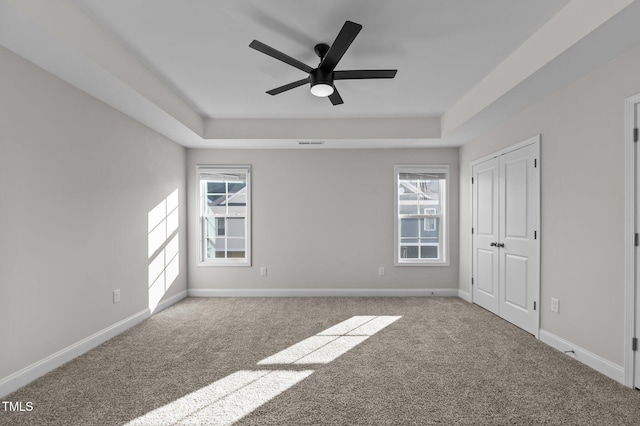 carpeted spare room featuring baseboards, visible vents, a tray ceiling, and ceiling fan