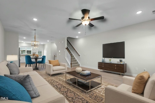 living area featuring light wood-style flooring, stairs, ceiling fan with notable chandelier, and recessed lighting