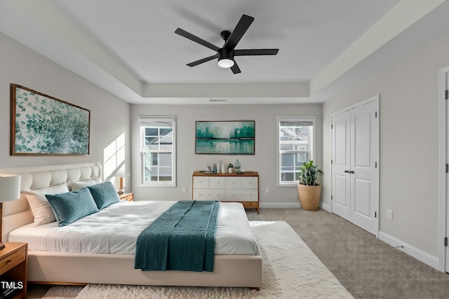 carpeted bedroom with multiple windows, baseboards, and a raised ceiling