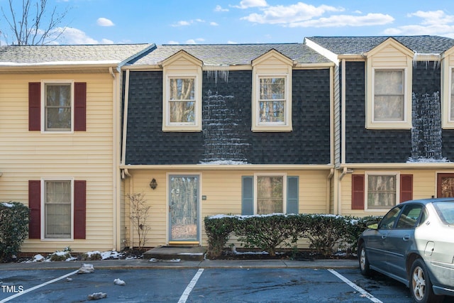 multi unit property featuring uncovered parking, mansard roof, and roof with shingles