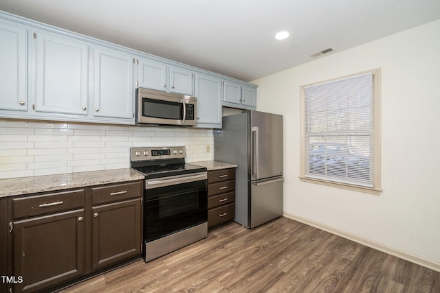 kitchen featuring dark brown cabinetry, wood finished floors, visible vents, appliances with stainless steel finishes, and tasteful backsplash