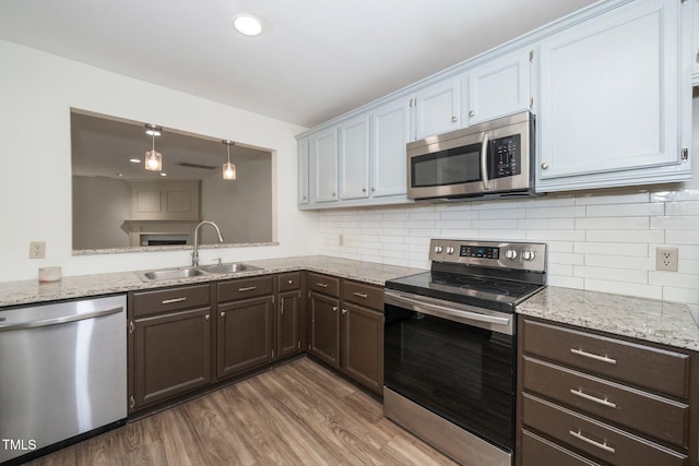 kitchen featuring appliances with stainless steel finishes, wood finished floors, decorative light fixtures, dark brown cabinets, and a sink