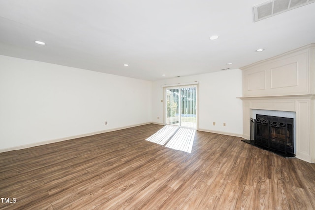 unfurnished living room with a fireplace with raised hearth, wood finished floors, visible vents, and baseboards