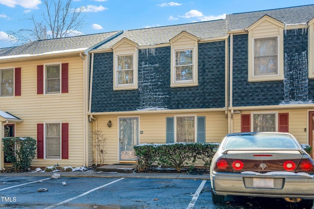 townhome / multi-family property with a shingled roof, uncovered parking, and mansard roof