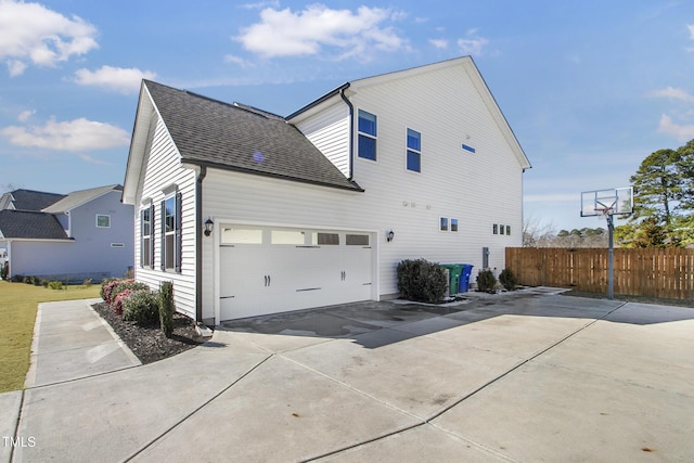 view of home's exterior with a garage, concrete driveway, roof with shingles, and fence