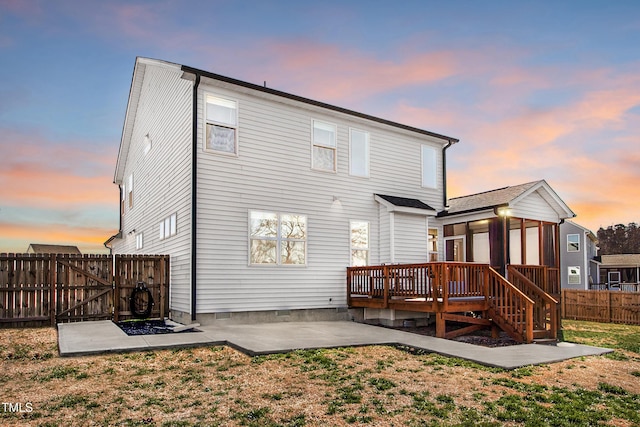 back of house at dusk featuring a wooden deck, a patio, a fenced backyard, a gate, and a yard