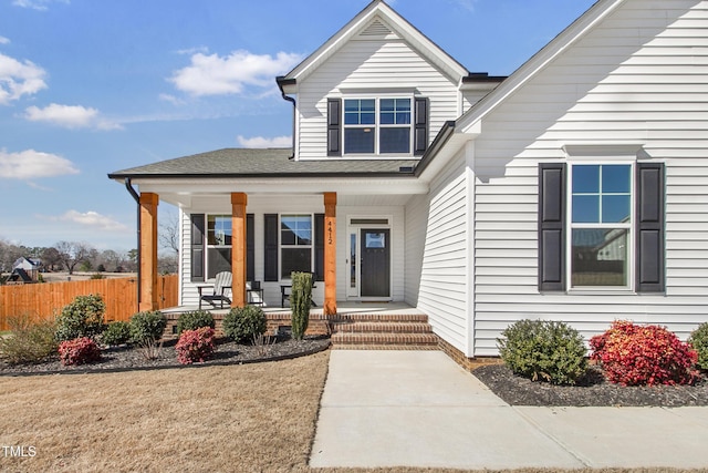 doorway to property featuring a porch, fence, and a shingled roof