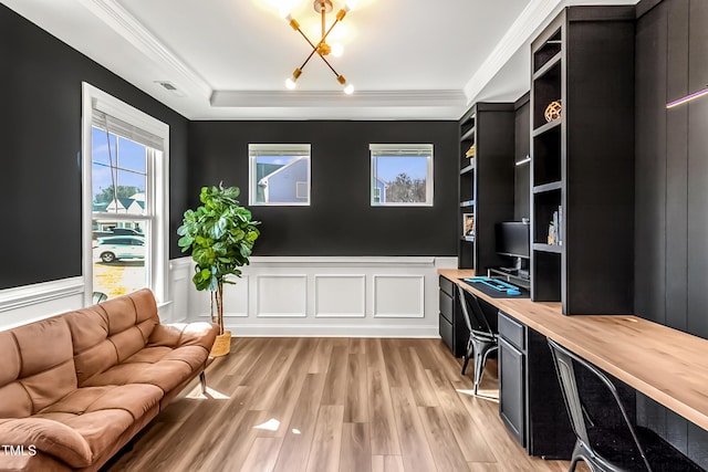 office with a chandelier, a wainscoted wall, light wood finished floors, built in desk, and crown molding