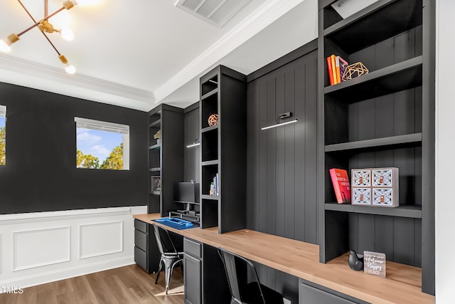 office featuring built in shelves, ornamental molding, wainscoting, built in study area, and light wood-type flooring