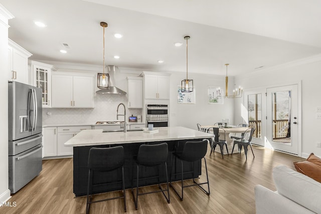 kitchen featuring stainless steel appliances, white cabinetry, wall chimney range hood, backsplash, and glass insert cabinets