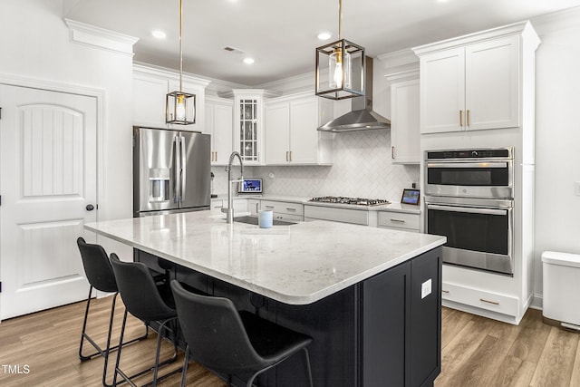 kitchen with light wood-type flooring, wall chimney exhaust hood, stainless steel appliances, and crown molding