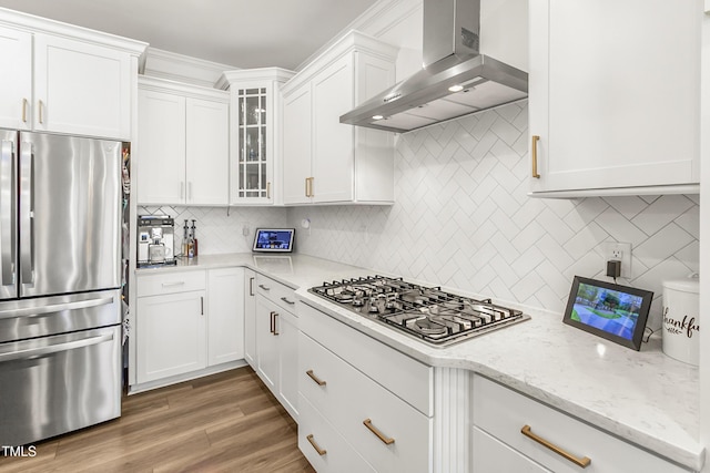 kitchen with stainless steel appliances, white cabinets, backsplash, wall chimney exhaust hood, and glass insert cabinets