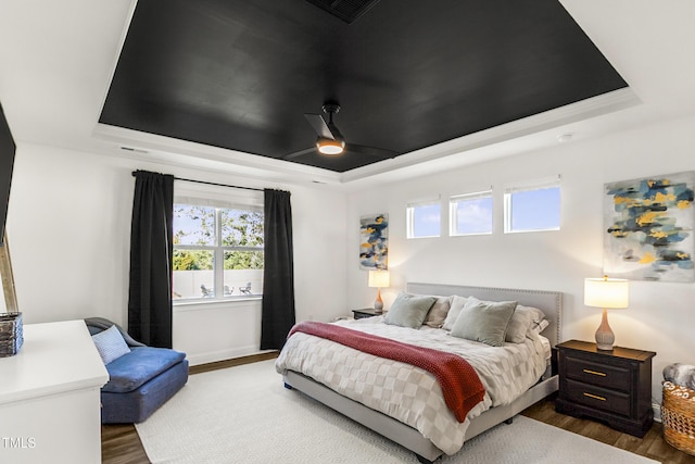 bedroom featuring wood finished floors, multiple windows, and a raised ceiling