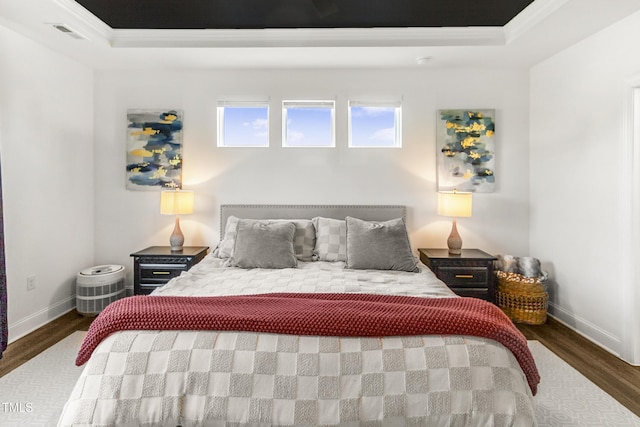 bedroom with baseboards, visible vents, a tray ceiling, and wood finished floors