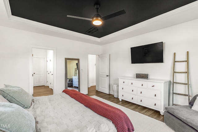 bedroom with a ceiling fan, a raised ceiling, visible vents, and wood finished floors