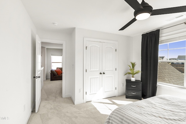 bedroom with a closet, light colored carpet, ceiling fan, and visible vents