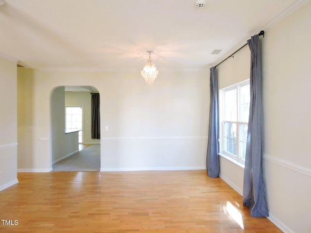 unfurnished room with light wood finished floors, a notable chandelier, arched walkways, and a wealth of natural light