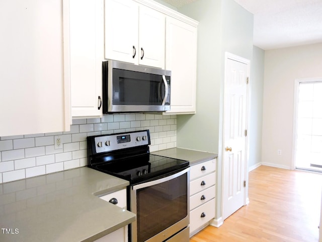 kitchen with baseboards, white cabinets, light wood-style flooring, stainless steel appliances, and backsplash