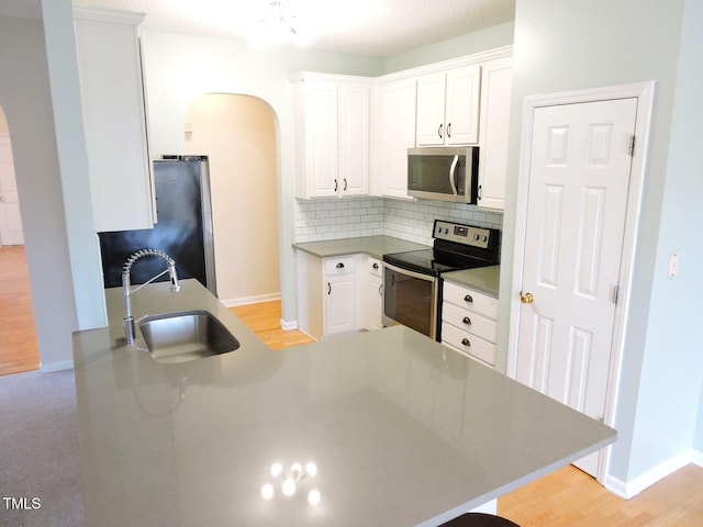 kitchen with arched walkways, stainless steel appliances, decorative backsplash, white cabinets, and a sink