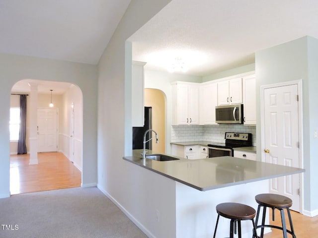 kitchen featuring arched walkways, a sink, a kitchen breakfast bar, appliances with stainless steel finishes, and decorative backsplash