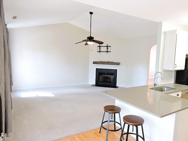 kitchen featuring a fireplace with flush hearth, white cabinets, vaulted ceiling, a sink, and ceiling fan