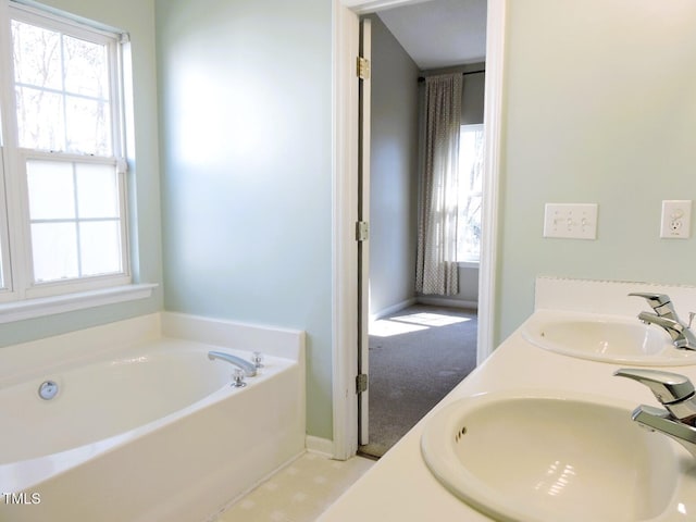 full bath with a garden tub, a sink, baseboards, and double vanity