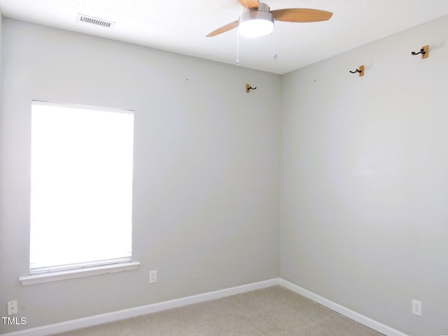 empty room featuring light carpet, ceiling fan, visible vents, and baseboards