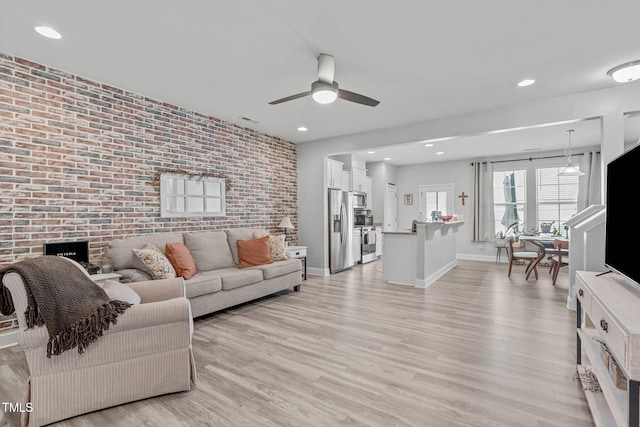 living area featuring recessed lighting, an accent wall, brick wall, light wood-type flooring, and baseboards