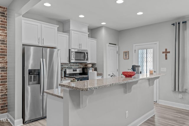 kitchen with light stone counters, a breakfast bar, tasteful backsplash, appliances with stainless steel finishes, and white cabinetry