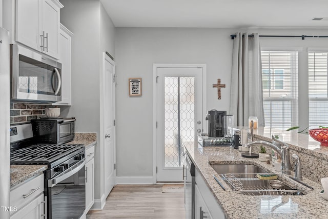 kitchen featuring visible vents, appliances with stainless steel finishes, light wood-type flooring, white cabinetry, and a sink