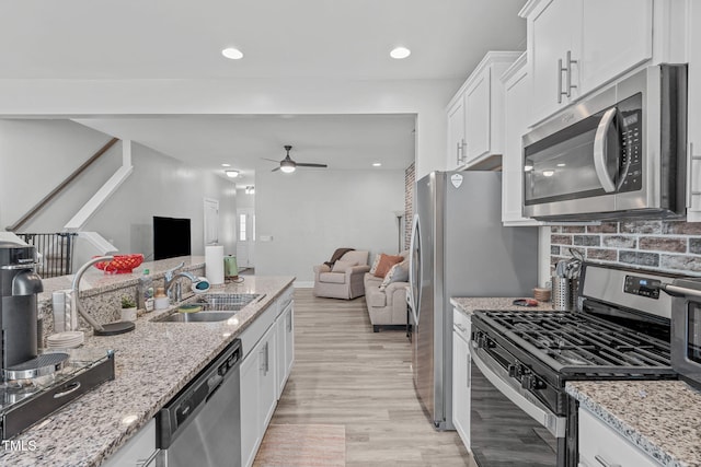 kitchen featuring stainless steel appliances, a ceiling fan, open floor plan, white cabinetry, and a sink