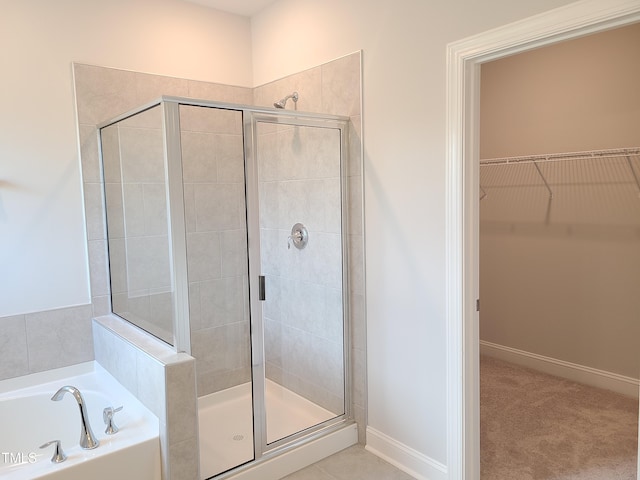 full bathroom featuring a walk in closet, a shower stall, baseboards, and a bath