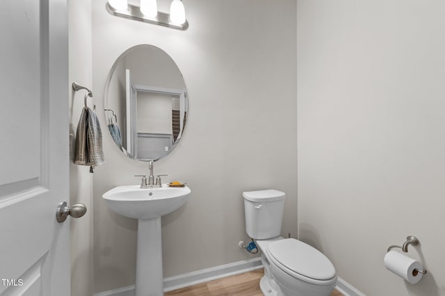 half bath featuring toilet, a sink, baseboards, and wood finished floors